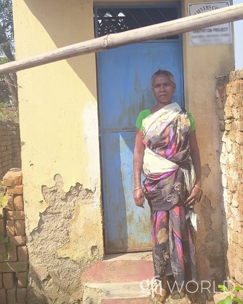 Woman stands in front of a sanitation facility that was provided through donors generous giving.
