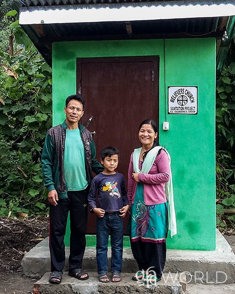 family stands in front of an outdoor toilet that was given to them.