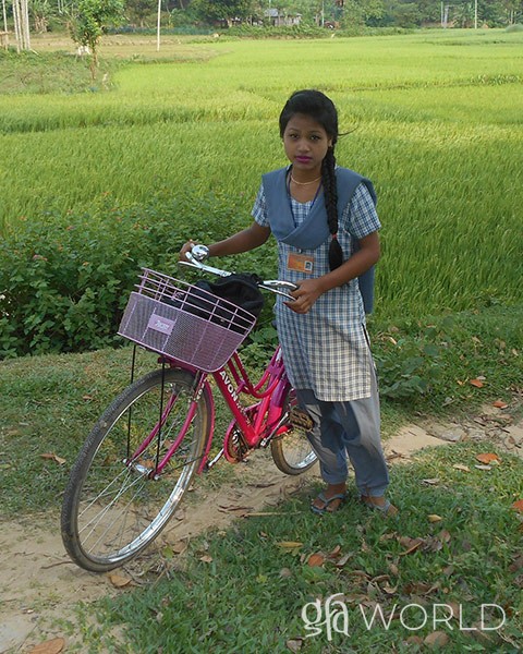 girl pictured in front of the bike she was given to go to school.