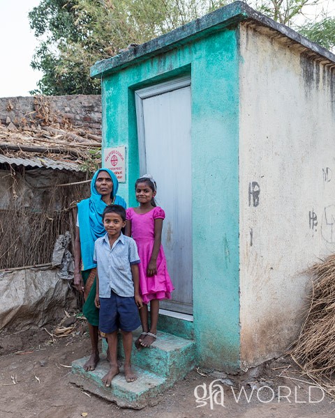 Family pictured in front of an outdoor toilet given to them by GFA World.