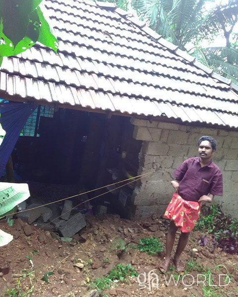 Man stands beside hole in his house caused by a landslide.