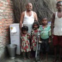 Man and his family stand beside the GFA World Biosand water filter.